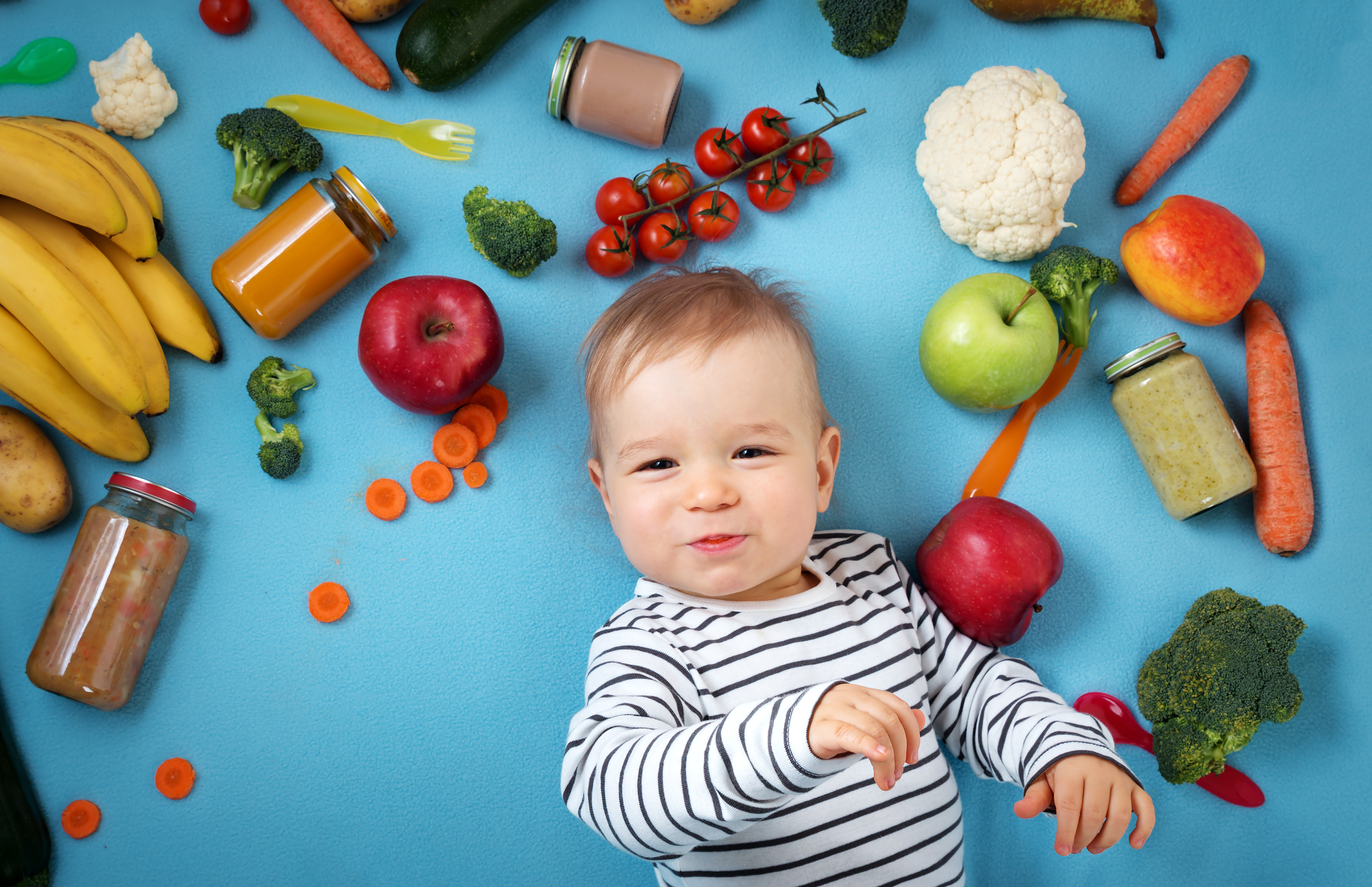 baby surrounded with fruits and vegetables on blue blanket, healthy child nutrition